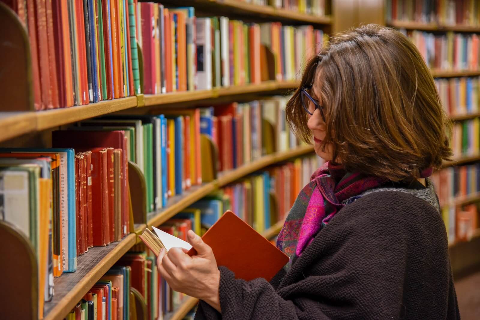 woman in red coat reading book in library